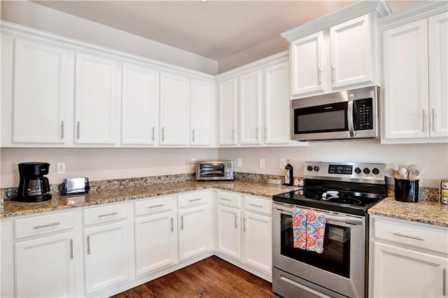 kitchen with stainless steel appliances, white cabinetry, light stone countertops, and dark wood-type flooring