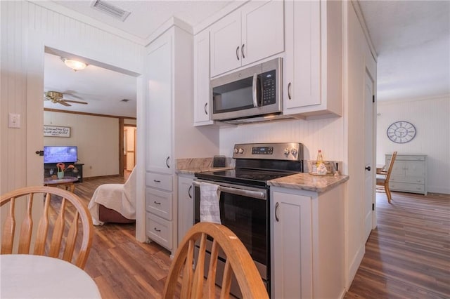 kitchen with appliances with stainless steel finishes, white cabinetry, ornamental molding, and wood-type flooring