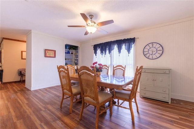 dining space with built in shelves, ceiling fan, crown molding, and wood-type flooring