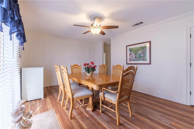 dining area with crown molding, ceiling fan, wood-type flooring, and a brick fireplace