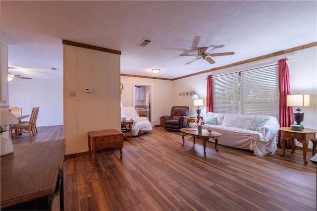 living room with a textured ceiling, ceiling fan, ornamental molding, and dark wood-type flooring