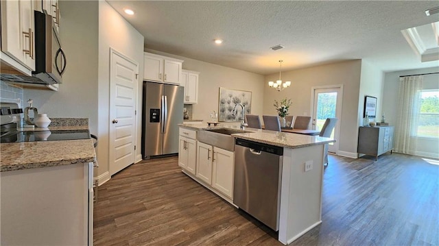 kitchen with sink, hanging light fixtures, appliances with stainless steel finishes, a kitchen island with sink, and white cabinets