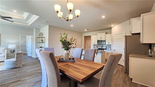 dining area with sink, hardwood / wood-style floors, ceiling fan with notable chandelier, and a raised ceiling