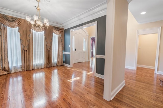 empty room featuring an inviting chandelier, ornamental molding, a wealth of natural light, and light wood-type flooring