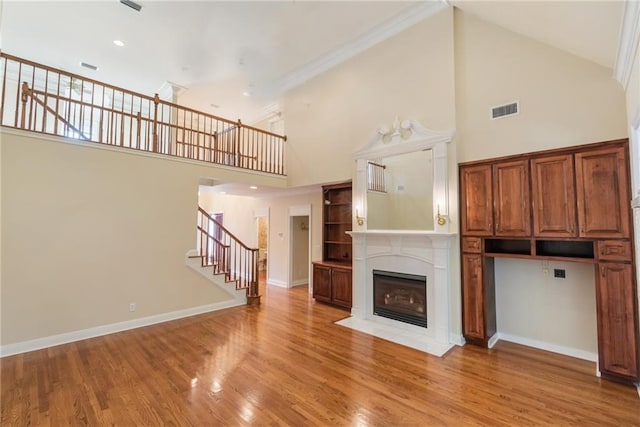 unfurnished living room featuring ornamental molding, a towering ceiling, and light wood-type flooring