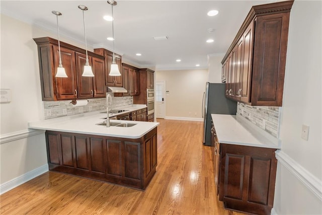 kitchen featuring decorative light fixtures, crown molding, backsplash, and light wood-type flooring