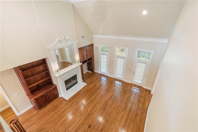 unfurnished living room with high vaulted ceiling, a tile fireplace, and light hardwood / wood-style flooring