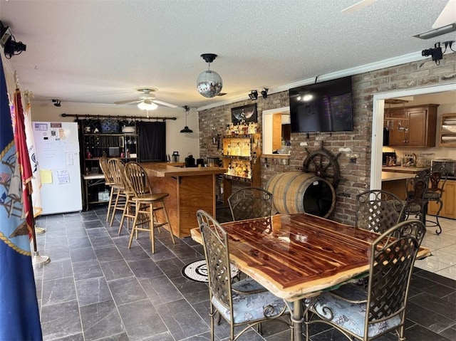 dining room with ceiling fan, crown molding, brick wall, and a textured ceiling