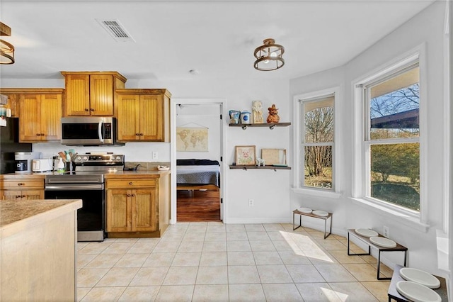 kitchen featuring light tile patterned flooring, stainless steel appliances, visible vents, light countertops, and brown cabinetry