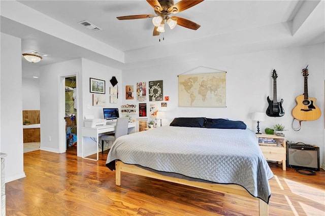 bedroom with a spacious closet, light wood-type flooring, a raised ceiling, and visible vents