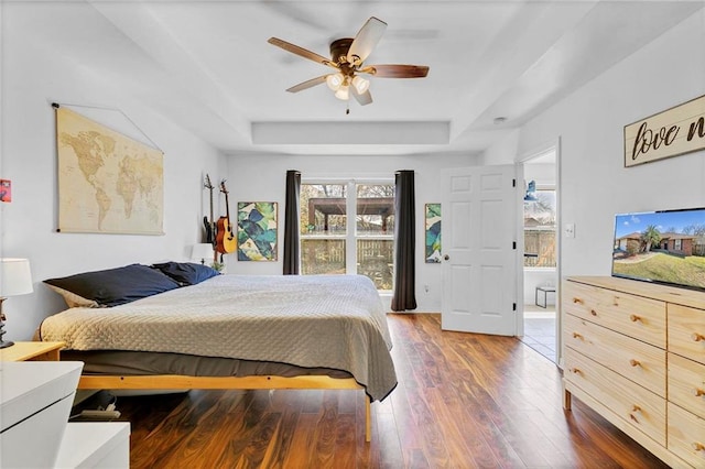 bedroom featuring a ceiling fan, a raised ceiling, multiple windows, and wood finished floors