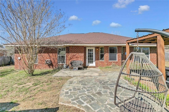 rear view of house with brick siding, roof with shingles, a patio area, and fence