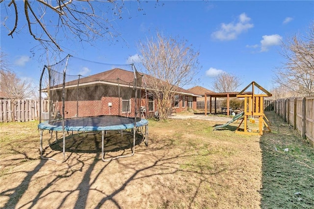 rear view of house featuring brick siding, a trampoline, a playground, and a fenced backyard