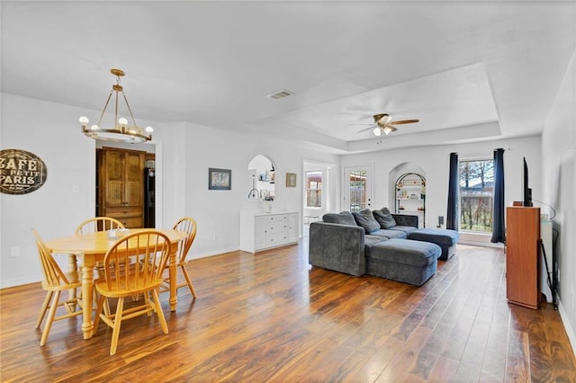 living room with a raised ceiling, visible vents, wood finished floors, baseboards, and ceiling fan with notable chandelier