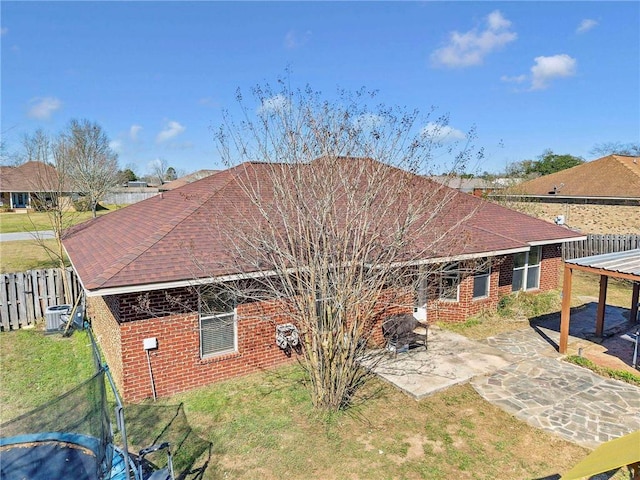 rear view of house with brick siding, a shingled roof, fence, a yard, and a patio area