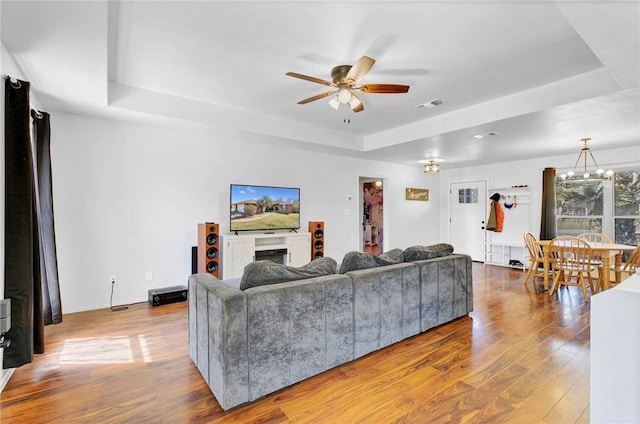 living room featuring ceiling fan with notable chandelier, a fireplace, wood finished floors, visible vents, and a raised ceiling