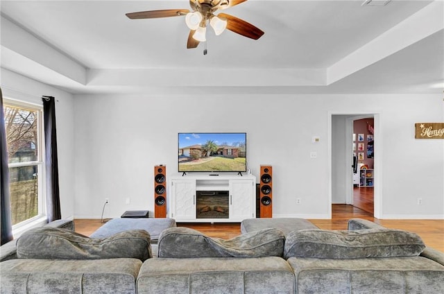 living area featuring a fireplace, baseboards, a raised ceiling, and wood finished floors