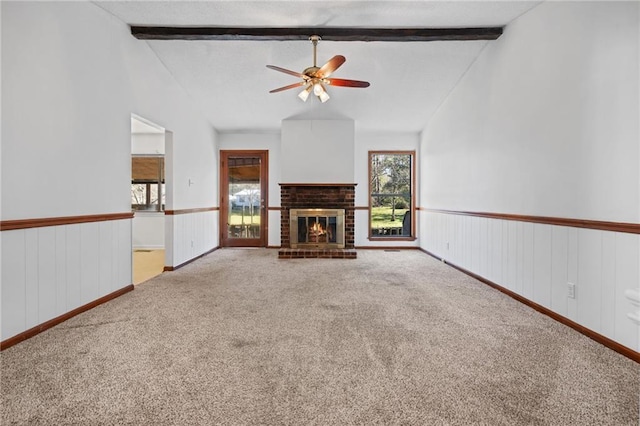 unfurnished living room with vaulted ceiling with beams, a brick fireplace, carpet flooring, and wainscoting