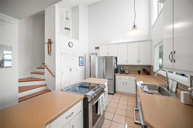 kitchen with light tile patterned floors, stainless steel appliances, a sink, white cabinets, and light countertops