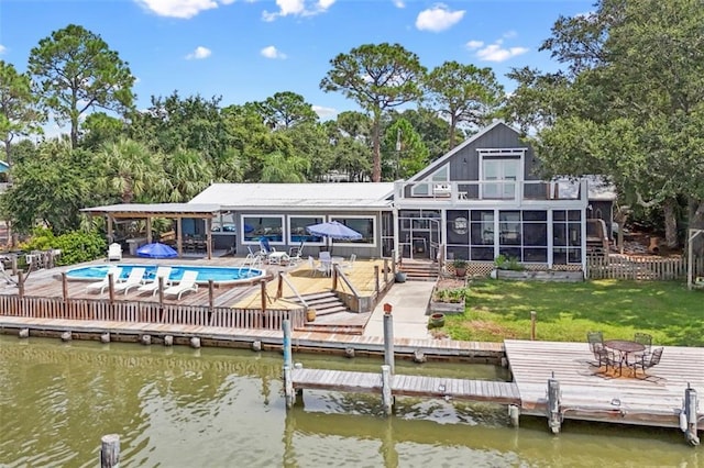 back of house with a deck with water view, fence, a sunroom, a lawn, and an outdoor pool