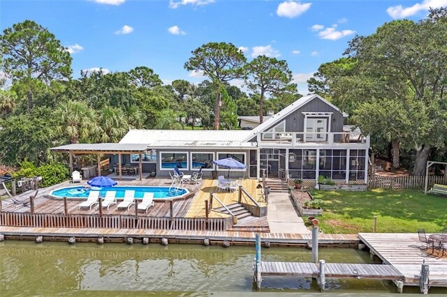 rear view of house featuring a lawn, a water view, fence, and a sunroom