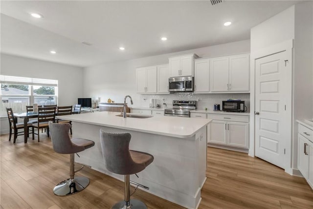 kitchen with a kitchen island with sink, sink, light wood-type flooring, appliances with stainless steel finishes, and white cabinetry