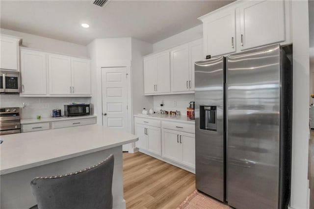 kitchen with a kitchen breakfast bar, tasteful backsplash, light hardwood / wood-style floors, white cabinetry, and stainless steel appliances