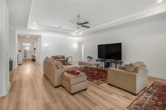 living room with light wood-type flooring, a raised ceiling, and ceiling fan