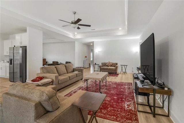 living room featuring ceiling fan, a raised ceiling, and light hardwood / wood-style flooring