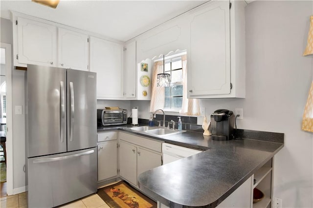 kitchen featuring a toaster, dark countertops, freestanding refrigerator, white cabinetry, and a sink