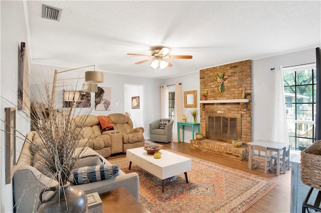 living area with visible vents, a fireplace, a textured ceiling, and wood finished floors