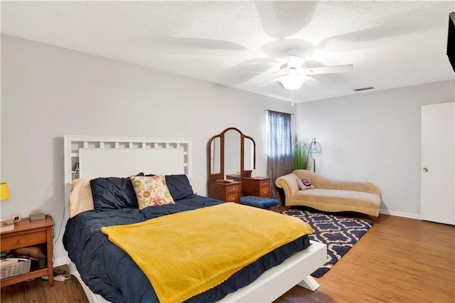 bedroom with a textured ceiling, wood finished floors, visible vents, baseboards, and a ceiling fan