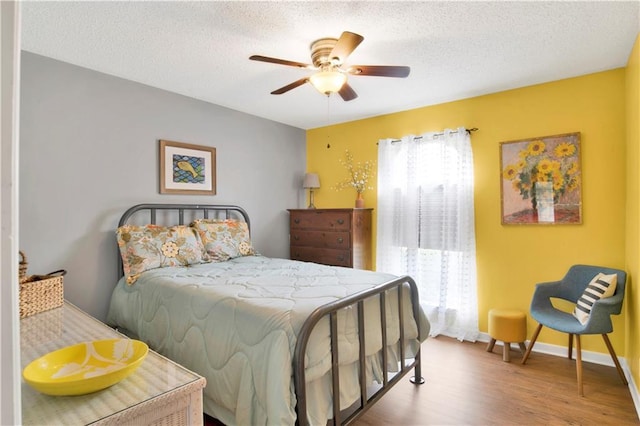 bedroom featuring a ceiling fan, a textured ceiling, baseboards, and wood finished floors