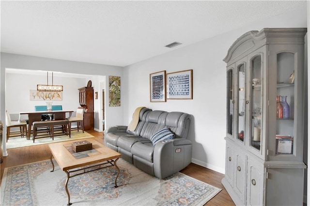 living room featuring a chandelier, dark wood-style flooring, visible vents, and baseboards