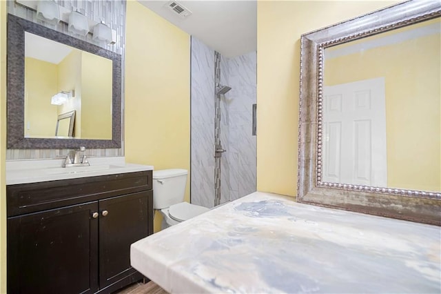 bathroom with a tile shower, vanity, and toilet