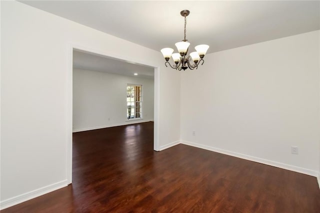 empty room featuring baseboards, dark wood-style flooring, and an inviting chandelier