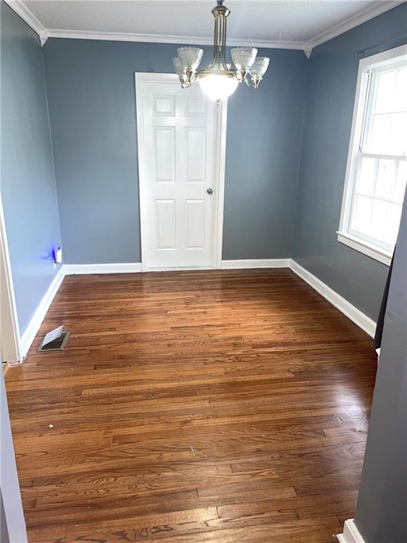 empty room featuring crown molding, wood finished floors, an inviting chandelier, baseboards, and visible vents