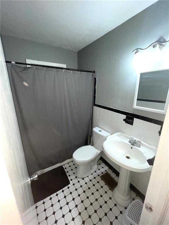 bathroom with toilet, a sink, tile walls, wainscoting, and a shower with shower curtain