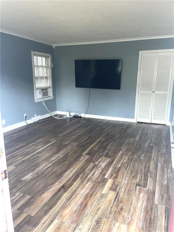 unfurnished living room with wood finished floors, a textured ceiling, crown molding, and baseboards