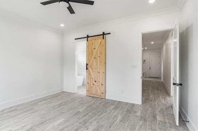 unfurnished bedroom featuring light hardwood / wood-style floors, ceiling fan, a barn door, ornamental molding, and connected bathroom