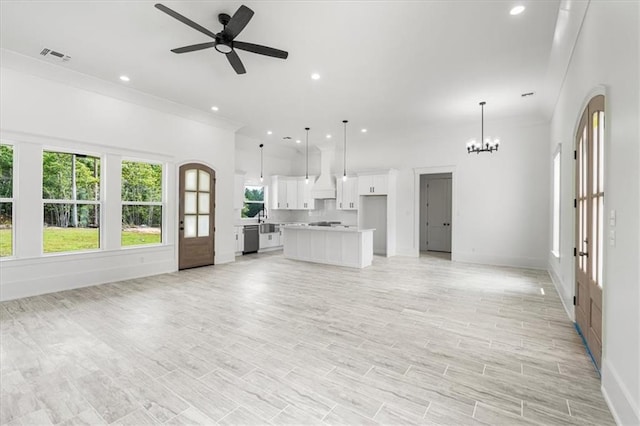 unfurnished living room featuring sink, ornamental molding, and ceiling fan with notable chandelier