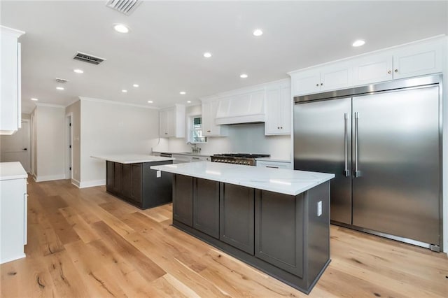 kitchen with built in fridge, visible vents, a kitchen island, and custom exhaust hood