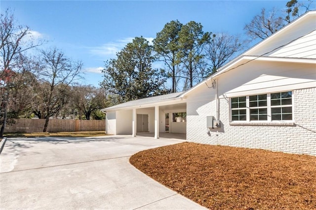 entrance to property featuring an attached carport, concrete driveway, brick siding, and fence