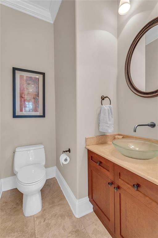 half bathroom with tile patterned flooring, toilet, vanity, baseboards, and ornamental molding