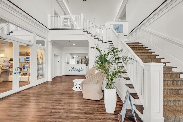 entrance foyer with a decorative wall, wood finished floors, a towering ceiling, stairs, and french doors