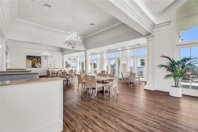 dining area with a notable chandelier, dark wood-style flooring, a tray ceiling, decorative columns, and crown molding