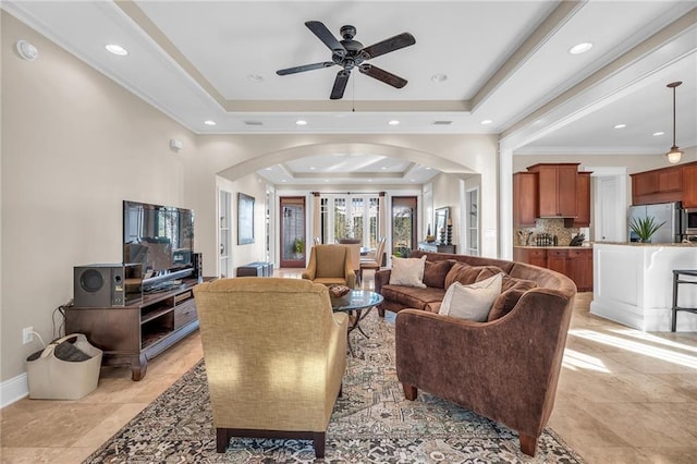 living room featuring arched walkways, crown molding, recessed lighting, a raised ceiling, and baseboards