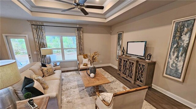 living area with crown molding, ceiling fan, a raised ceiling, baseboards, and wood finished floors