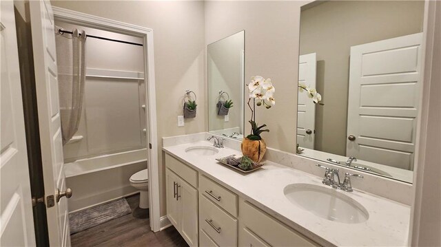 bathroom with a sink, double vanity, toilet, and wood finished floors