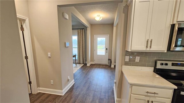 kitchen with decorative backsplash, appliances with stainless steel finishes, dark wood finished floors, baseboards, and white cabinets